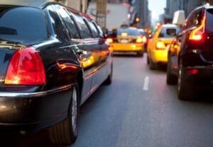 Black sedan in the foreground on a busy city street with red tail lights in heavy traffic ahead